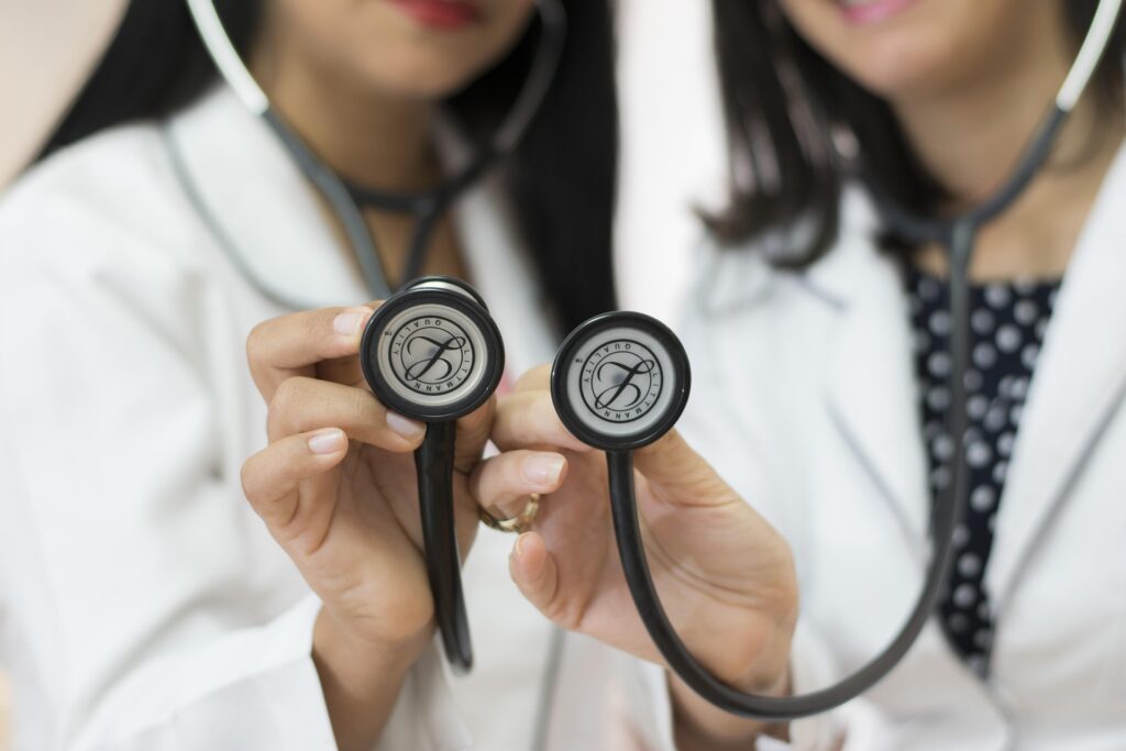 Two providers in white coats hold stethoscopes side by side.