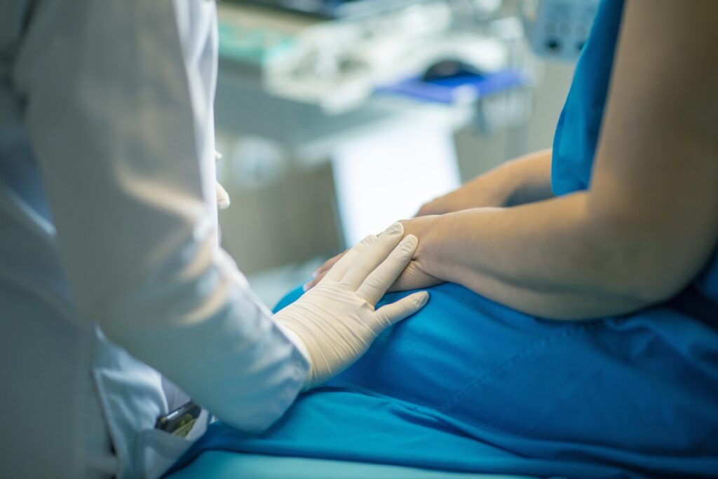 A care provider's gloved hand touches the arm of a patient in a reassuring gesture.